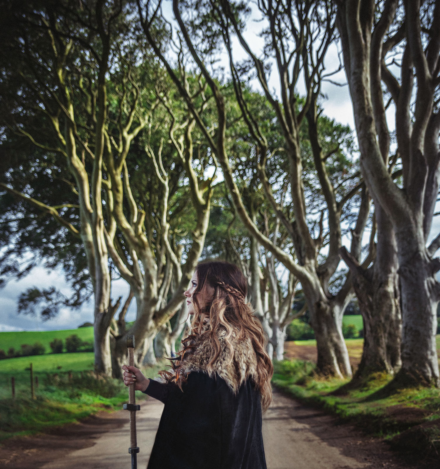 Woman with cape and sword standing under The Dark Hedges in Northern Ireland