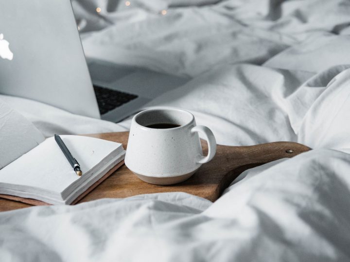 Cutting board, coffee cup and Macbook in a bed with grey sheets