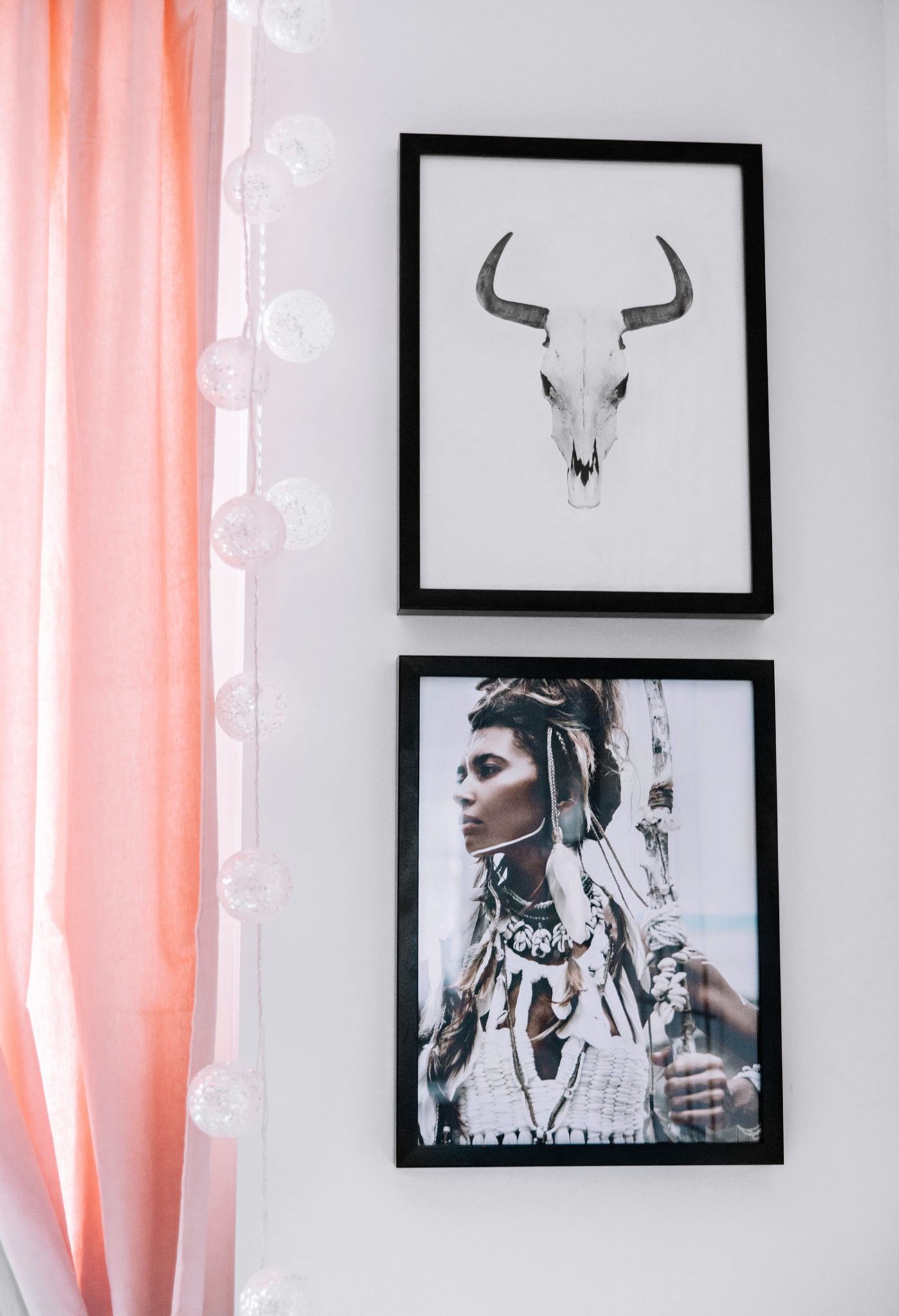 Two boho posters hanging next to window with pink curtains