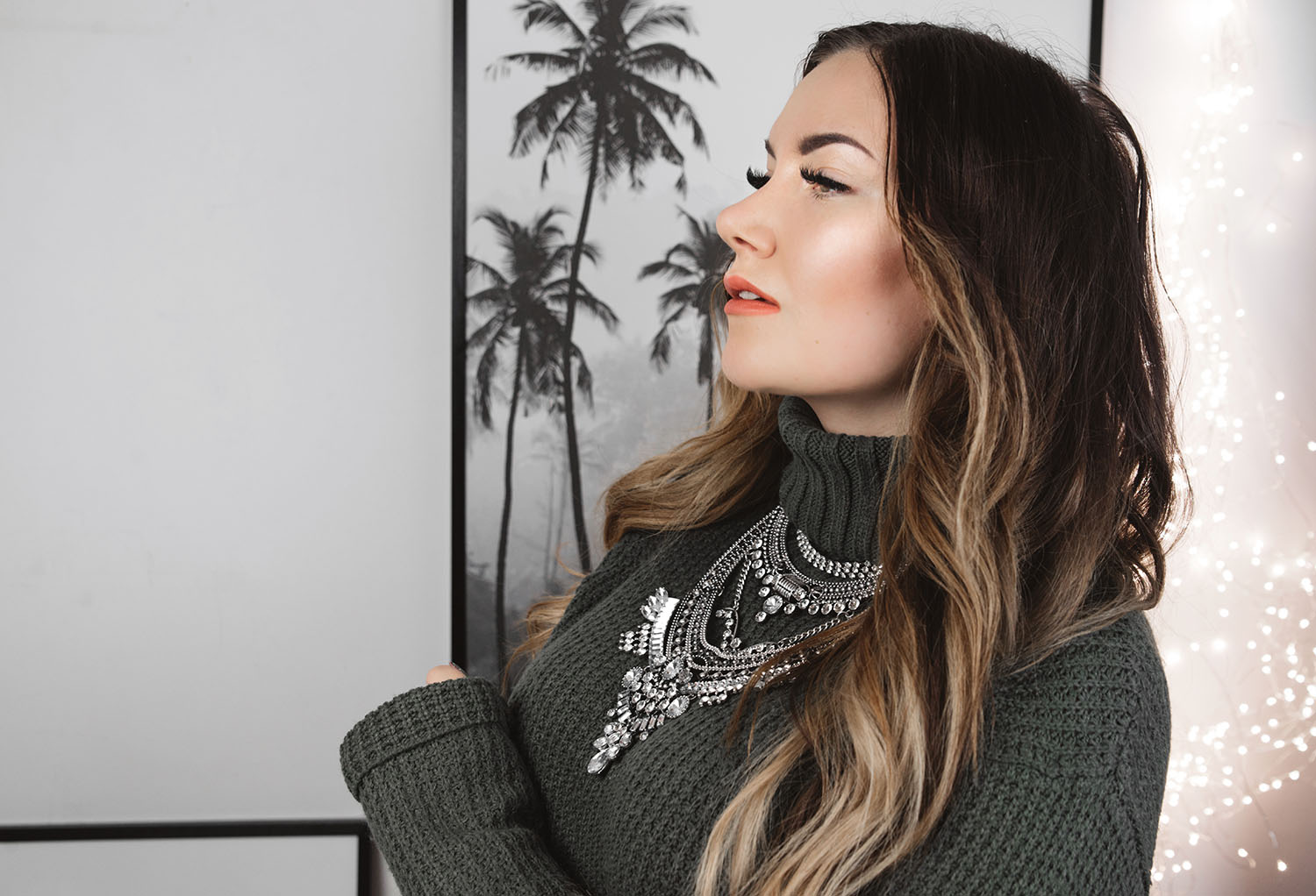 Woman wearing statement necklace standing in front of poster with palm trees