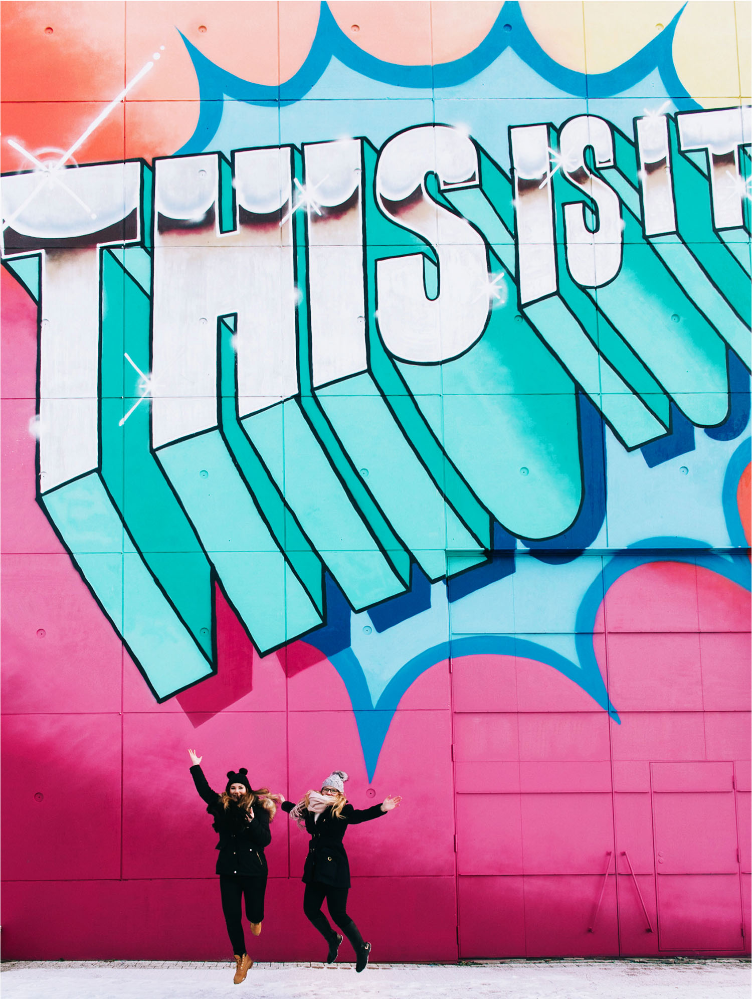 Two women jumping in front of "This is it" street art at Myyrmäki railway station