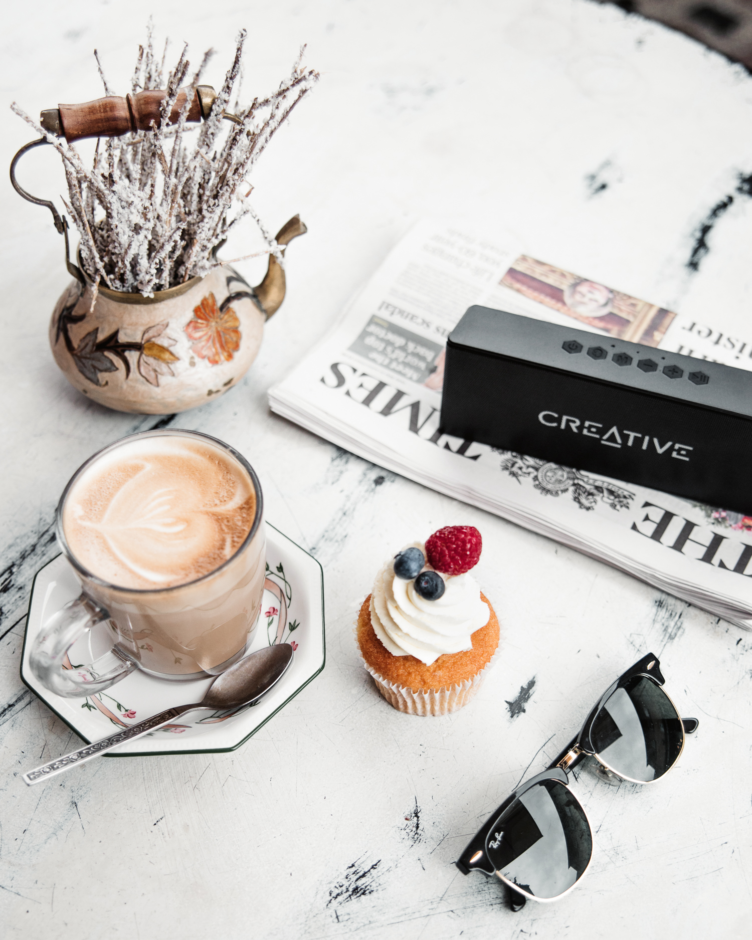 Flatlay med kaffe, bakverk, tidning och högtalare från Creative