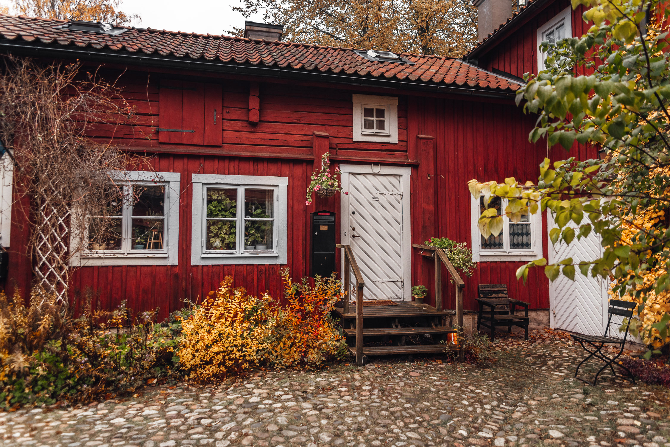 Rött trähus omringat av färgglada höstlöv i Wadköping friluftmuseum i Örebro