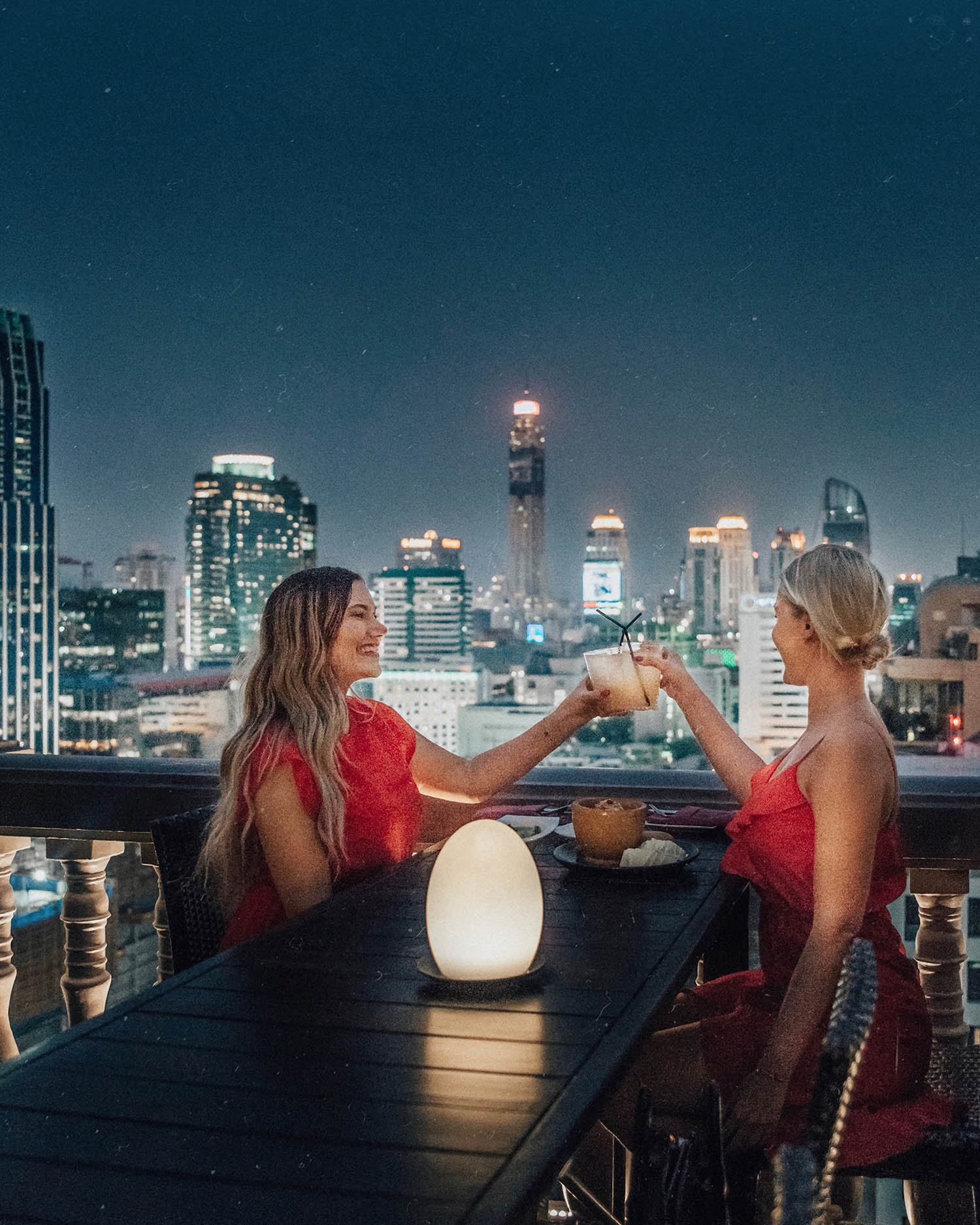 Two girls in red dresses sharing a toast - Rooftop Bar at Muse Hotel in Bangkok, Thailand