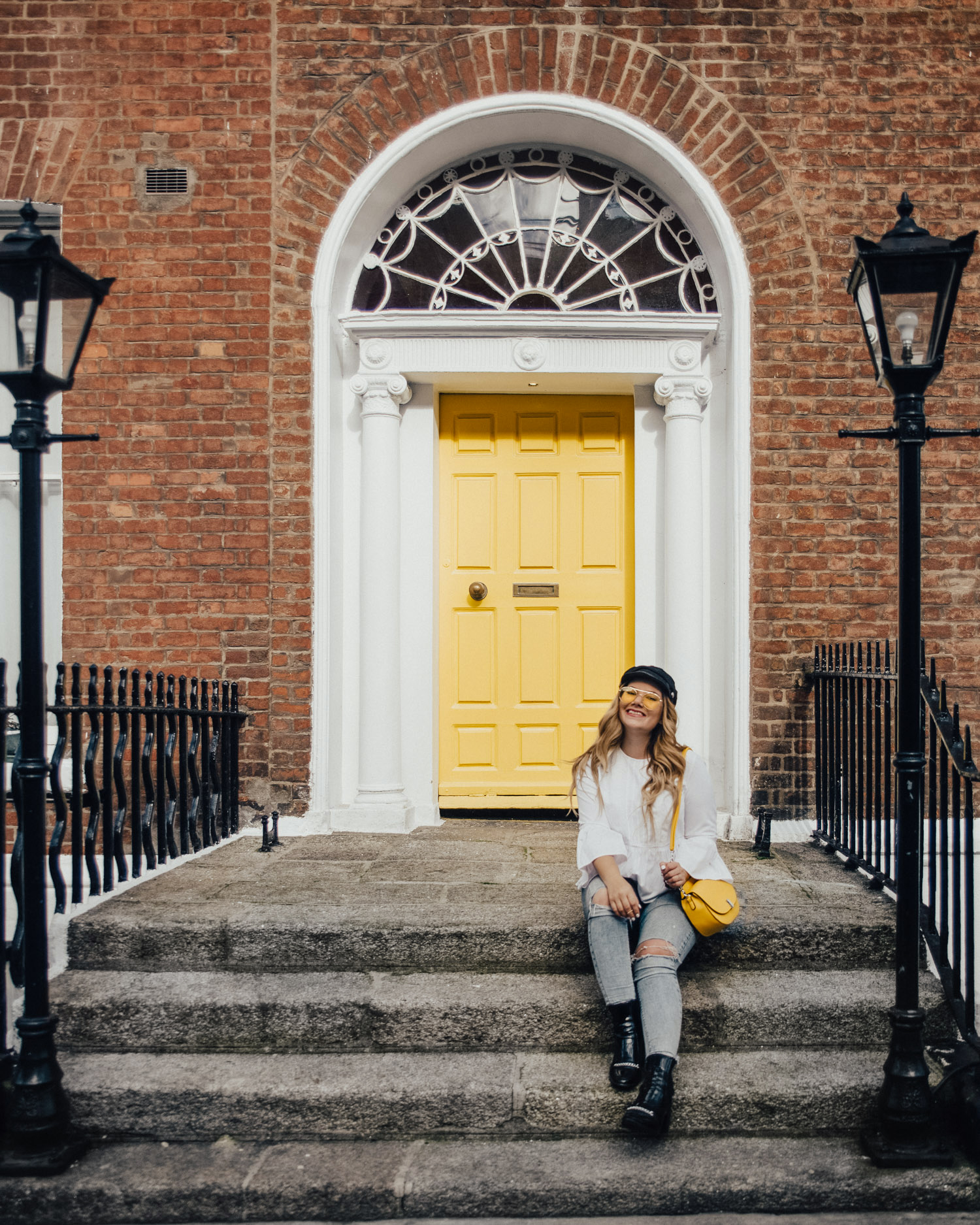Woman with cap and yellow bag sitting by Georgian Yellow Door in Dublin, Ireland